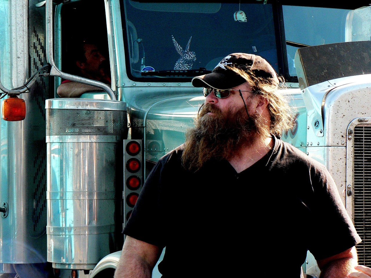 Bearded owner-operator standing beside his semi-truck cab